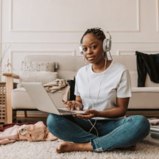 black girl sitting crosslegged using a laptop and wearing headphones