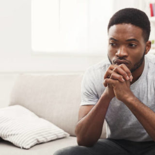 Young african-american man sitting at home. Sad guy sitting on the couch